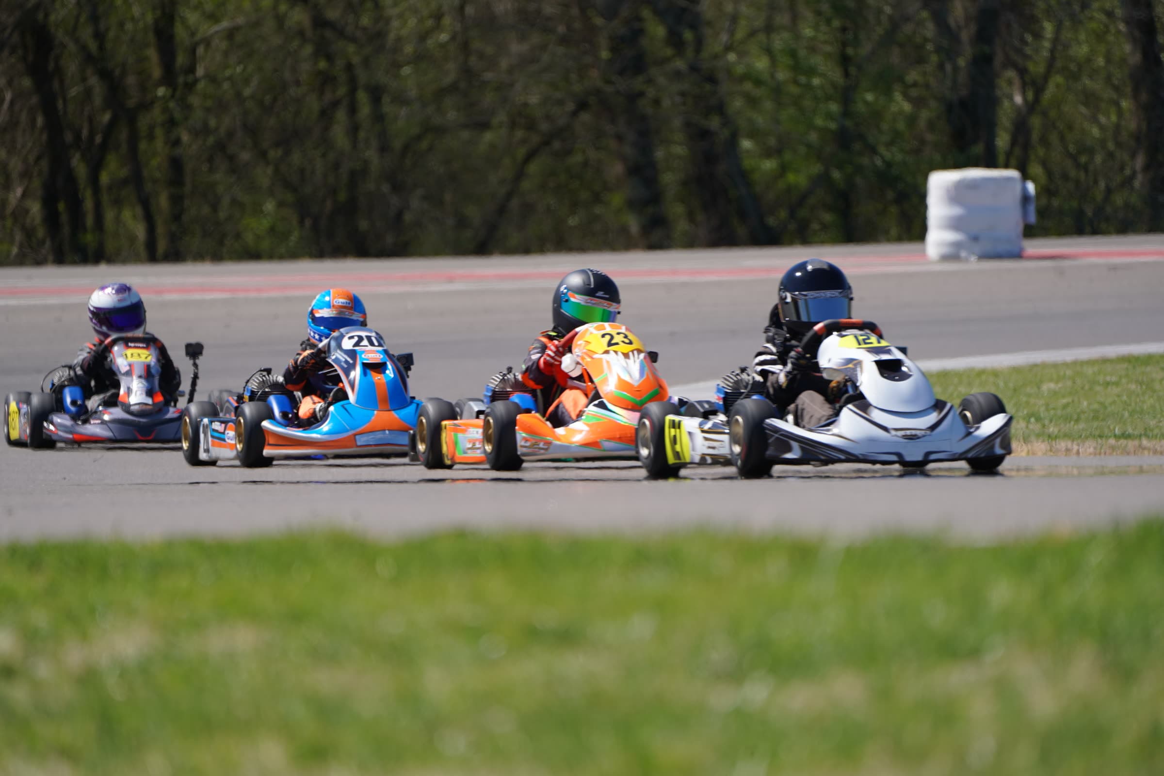 Four owner karts from different classes racing wheel to wheel through a corner