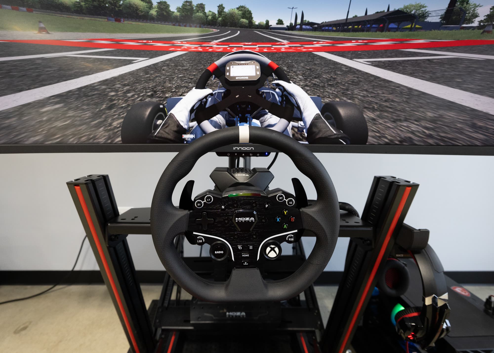 A Music City Kartplex sim rig: direct-drive wheel and curved ultrawide screen running Assetto Corsa